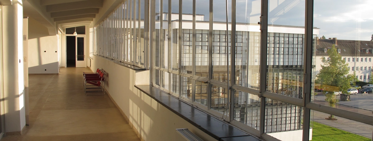 This image shows an interior hallway with a large glass curtain wall inside the iconic Bauhaus Dessau building in Germany, designed by Walter Gropius